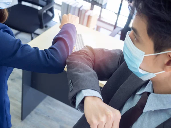 Elbow bump. Businessman and business woman wearing protective face mask and use elbow to bump into greeting. Safe greetings. New way to greet, instead of shaking hands to avoid spread of coronavirus.