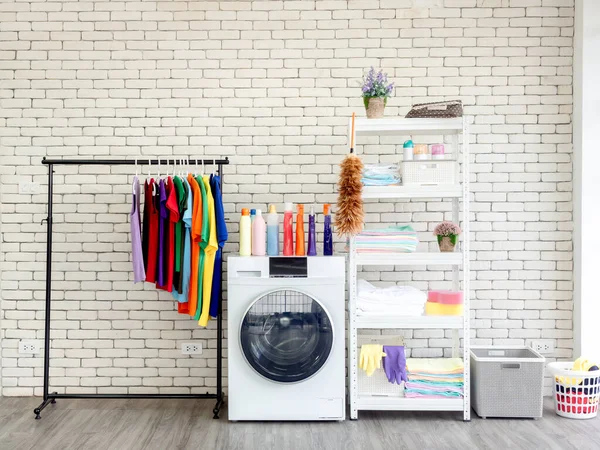 Laundry room interior. Utility room with washing machine, cleaning equipment, various home cleaner, clean wipes and colorful clothes hanging on the clothesline on white vintage brick wall background.