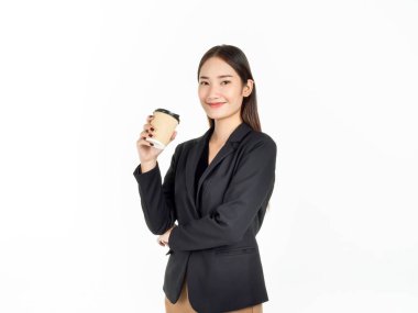 Takım elbiseli, gülümseyen genç Asyalı iş kadını beyaz arka planda izole edilmiş kahve içiyor. Tek kullanımlık kağıt kahve fincanı tutan çekici iş kadını portresi..