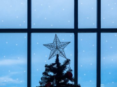 Karanlık Noel ağacının tepesinde büyük bir yıldız pencere camının yanında mavi gökyüzü arka planında karla kaplı, kış mevsiminde yalnız hisseden..