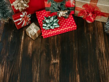 Noel ve mutlu yıllar. Parlak yeşil, kırmızı ve altın renkli bir sürü hediye kutusu var. Koyu ahşap arka planda, parlak yeşil, kırmızı ve altın yay süslemeleri var..