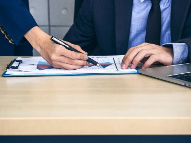 İş adamı ve kadının elleri çalışma masasındaki not çizelgesini ve bilgisayarı kontrol ediyor, ofiste fotokopi uzayı ile buluşuyor ve birlikte çalışıyorlar..