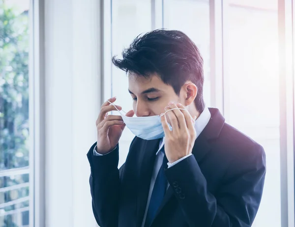 Young Asian businessman in suit wearing medical face mask in office, new normal working lifestyle after coronavirus pandemic lockdown.