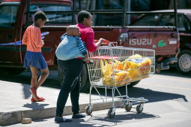 Johannesburg, Güney Afrika - 4 Eylül, 2018: alışveriş sepeti iterek sırtında bebek ile anne.