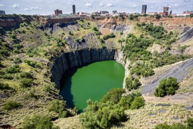Kimberley, South Africa, 10th April -2019: View of open pit mine with lake. City in background. clipart