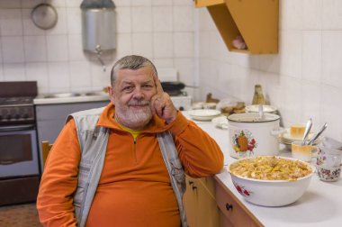 Mutfakta bir sandalyede oturan sakallı üst düzey adam portresi