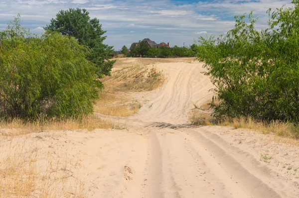 Landscape with sandy track leading to human settlement