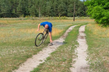 Kapalı olgun adam bir ülke yolda eski bir bisiklet üzerinde düşme anı