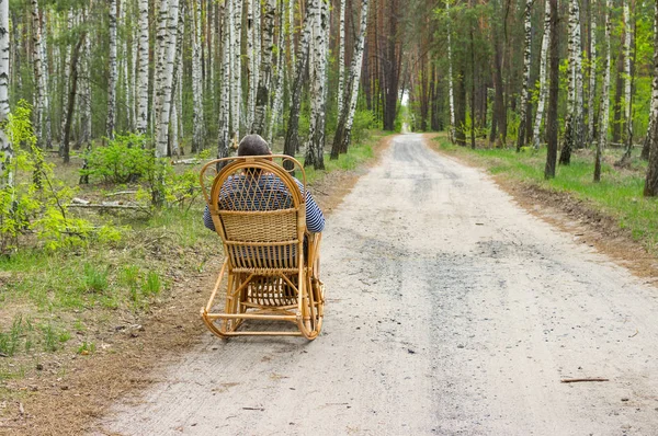 Elderly man is having rest in forest sitting on a wicker rocking-chair