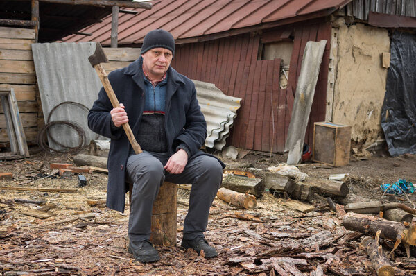 Mature man with an axe sitting on a log