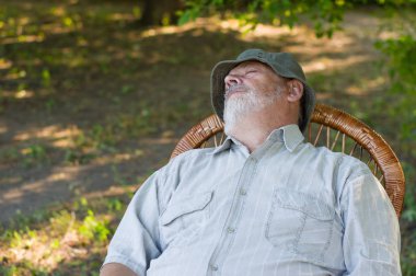 Outdoor portrait of Caucasian senior man sleeping in a wicker chair in summer park clipart
