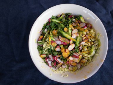 Buruşuk mavimsi pamuklu kumaş üzerinde duran bahar sebze salatası için malzemelerile kase üzerinde üst görünümü