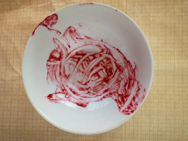 Empty bowl with raspberry mash leftovers standing on crumped graph paper surface — Stock Photo, Image