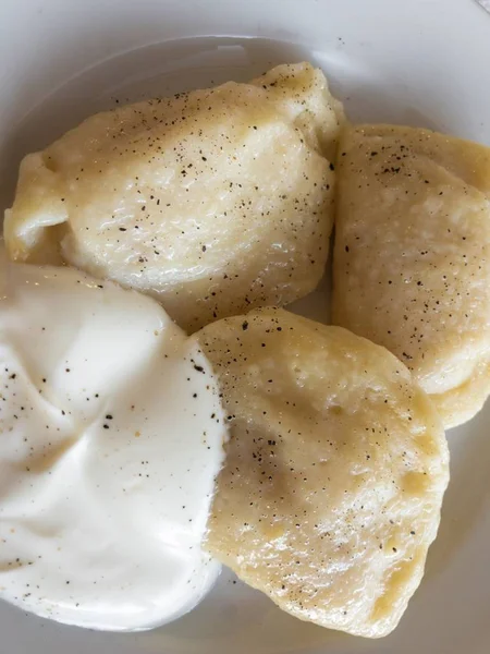 Bord met drie Oekraïense vareniky gevuld met aardappelpuree, op smaak gebracht met zwarte peper en geserveerd met zure room — Stockfoto