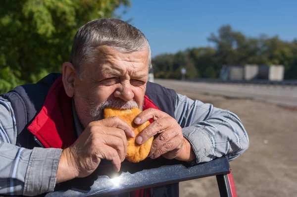 Portrait of hungry senior driver eating patty leaning his elbows on his car door