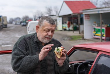 Ukrayna 'da bir arka yolda dikilirken arabasının yanında sokak yemeği (lahanada lyulya kebabı) taşıyan kıdemli sürücü