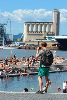 Oslo, Norveç - 26 Haziran 2018: Adam yüzme ve bir sıcak yaz gününde Oslo'nun liman mesire Sorenga plajda güneşlenirken insanların resmini alıyor.