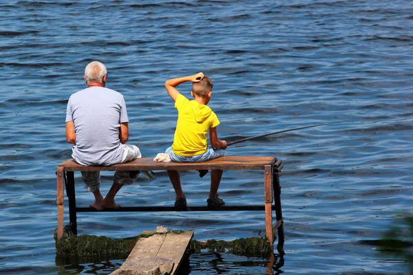 Old man and a boy sit on a self-made fishing platform with rods