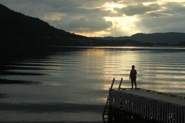 Kadın Bisiklet kask içinde ahşap bir iskele üzerinde duruyor ve Dimmelsvik, Norveç'te batımında görünüyor
