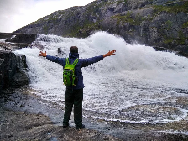 Man looks at Nykkjesoyfossen falls, the third in cascade of four waterfalls at Husedalen valley, Kinsarvik, Norway