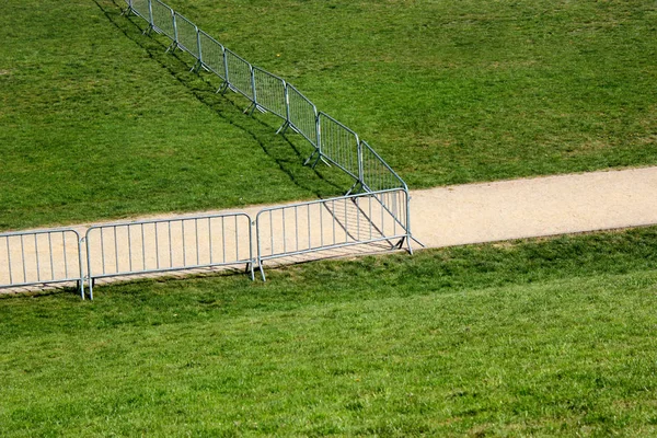 Un sendero sobre hierba verde detrás de una valla metálica móvil — Foto de Stock