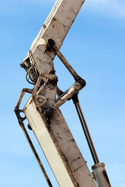 Velho pistão hidráulico gorduroso e sujo de retroescavadeira branca contra céu azul. Máquina pesada para escavação no canteiro de obras. Máquinas hidráulicas . — Fotografia de Stock