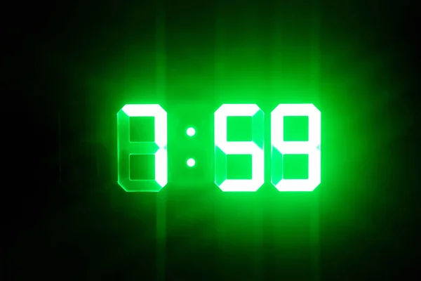 Green glowing digital clocks in the dark show 7: 59 time — стоковое фото