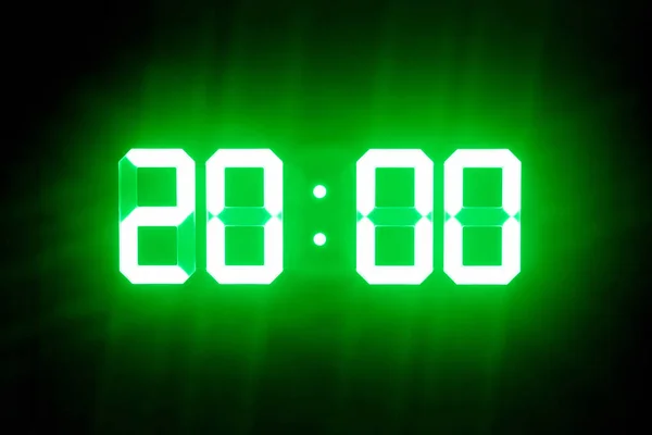 Green glowing digital clocks in the dark show 20: 00 time — стоковое фото