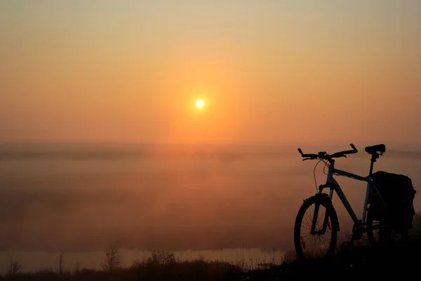 Fahrradtour bei Sonnenaufgang. Fahrrad, Morgennebel und orangefarbene Sonne. — Stockfoto