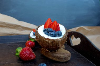 ahşap elemanları ile koyu bir arka plan üzerinde taze hindistan cevizi bir kase renkli taze çilek, yaban mersini ve diğer meyveler