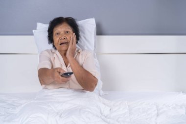 Son sınıf öğrencisi, yatağında uzaktan kumandayla korku filmi izliyor.