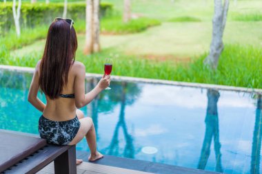Yüzme havuzunda şarap bardağını tutan genç kadın