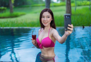 Kadın akıllı telefon kullanıyor ve yüzme havuzunda selfie çekiyor.