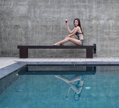 sandalyeye dinlenme ve yüzme havuzunda bir cam tutan kadın