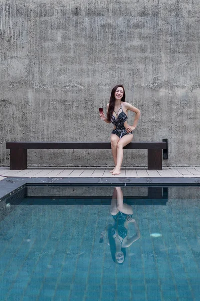 sandalyeye dinlenme ve yüzme havuzunda bir cam tutan kadın