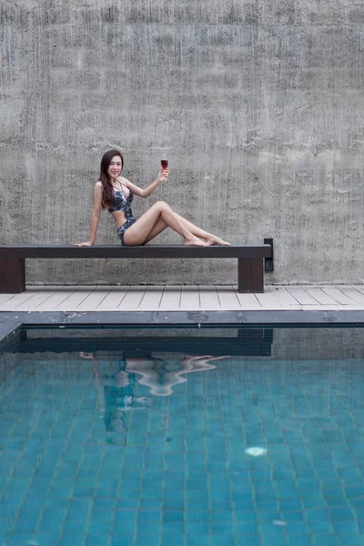 sandalyeye dinlenme ve yüzme havuzunda bir cam tutan kadın