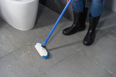 Banyodaki fayansları temizlemek için fırça kullanan el.