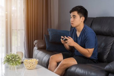 Genç adam oturma odasında joystick ile video oyunu oynuyor.