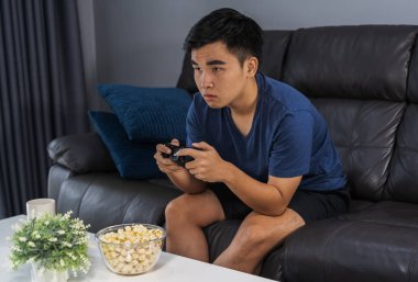 Genç adam oturma odasında joystick ile video oyunu oynuyor.