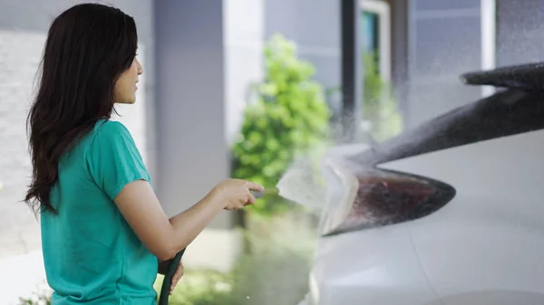 若い女性水スプレー洗浄水管と彼女の車 — ストック写真