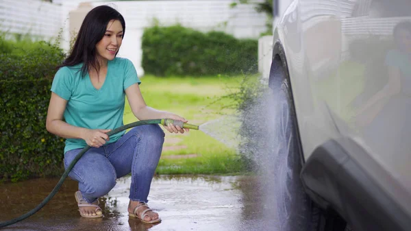 若い女性水スプレー洗浄水管と彼女の車のホイール — ストック写真