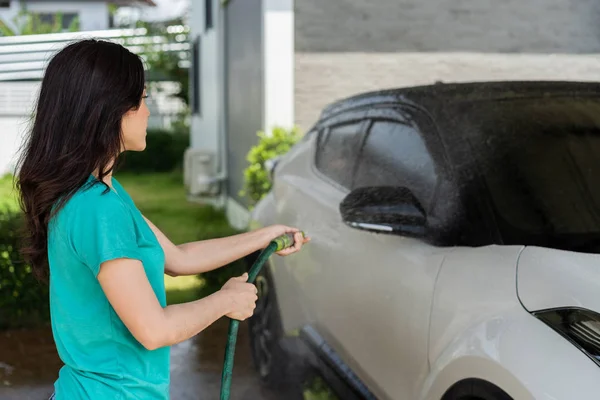 若い女性水スプレー洗浄水管と彼女の車 — ストック写真