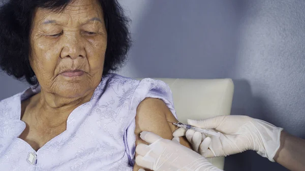 Doctor giving vaccine injection into senior woman shoulder