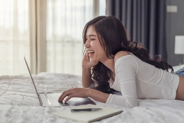 laughing young woman lying in bed and using a laptop computer