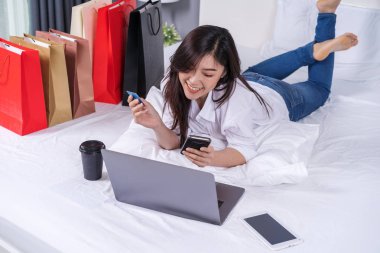 mutlu kadın yatağın üzerinde kredi kartı ile online alışveriş için Smartphone kullanarak
