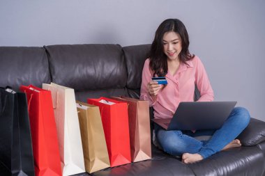 oturma odasında kredi kartı ile online alışveriş için dizüstü bilgisayar kullanan mutlu kadın
