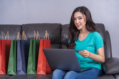 oturma odasında kredi kartı ile online alışveriş için dizüstü bilgisayar kullanan mutlu kadın