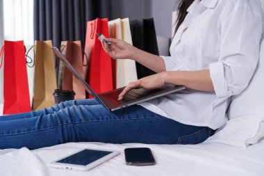 bir yatakta kredi kartı ile online alışveriş için dizüstü bilgisayar kullanan kadın