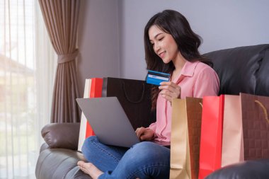 oturma odasında kredi kartı ile online alışveriş için dizüstü bilgisayar kullanan mutlu kadın