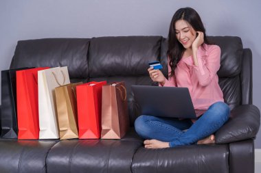oturma odasında kredi kartı ile online alışveriş için dizüstü bilgisayar kullanan mutlu kadın
